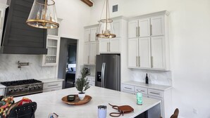 A modern kitchen with white cabinetry, a central island, stainless steel appliances, and pendant lighting. - Hillside Hideaway (Bokchito)