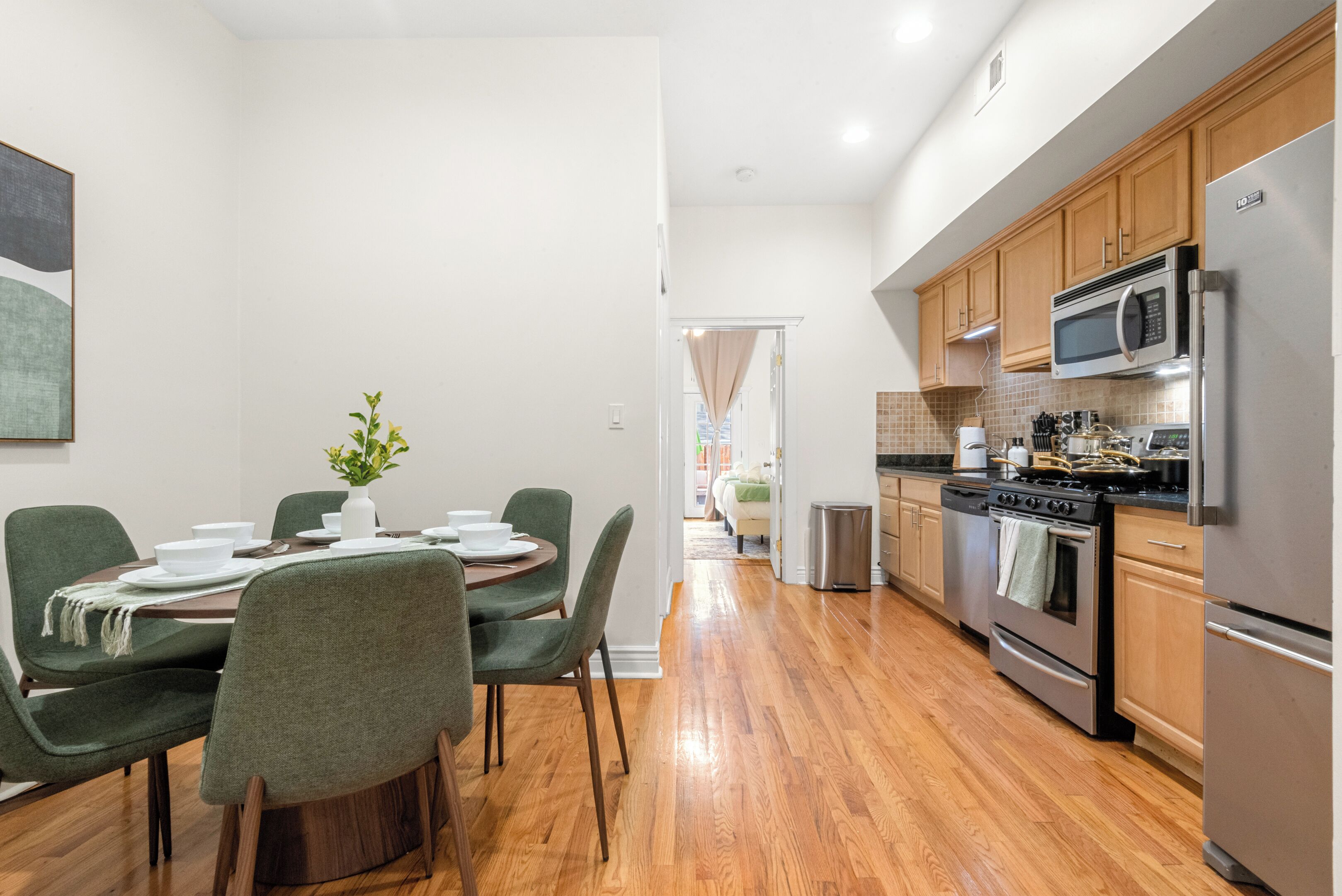 A modern kitchen with wooden cabinets, stainless steel appliances, and a dining area with green chairs and a table set for four.