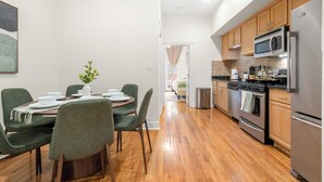 A modern kitchen with wooden cabinets, stainless steel appliances, and a dining area with green chairs and a table set for four. - Private Patio Apt • Min to NYC • Sleeps up to 9 • Free Parking • Washer/Dryer (Hoboken)