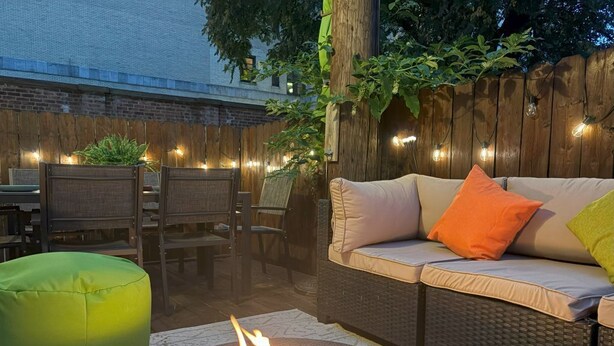 An outdoor patio with a round fire pit, wicker furniture, and string lights. - Private Patio Apt • Min to NYC • Sleeps up to 9 • Free Parking • Washer/Dryer (Hoboken)