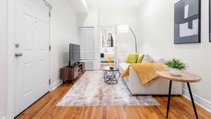 A modern living room with a sofa, coffee table, and a television. - Private Patio Apt • Min to NYC • Sleeps up to 9 • Free Parking • Washer/Dryer (Hoboken)