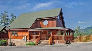 Une cabane en rondins avec un toit à forte pente, une grande fenêtre octogonale et une véranda dotée d’une balustrade.