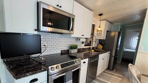 Eine moderne Küche mit weißen Schränken, einer Edelstahl-Mikrowelle, einem eingebauten Backofen und einem Flachbildfernseher.
