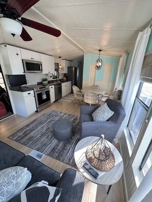 A compact living space with a kitchenette, a sofa set, a dining table, and a ceiling fan.