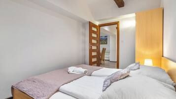 A bedroom with two beds, a wooden headboard, a bedside lamp, and a door leading to another room.