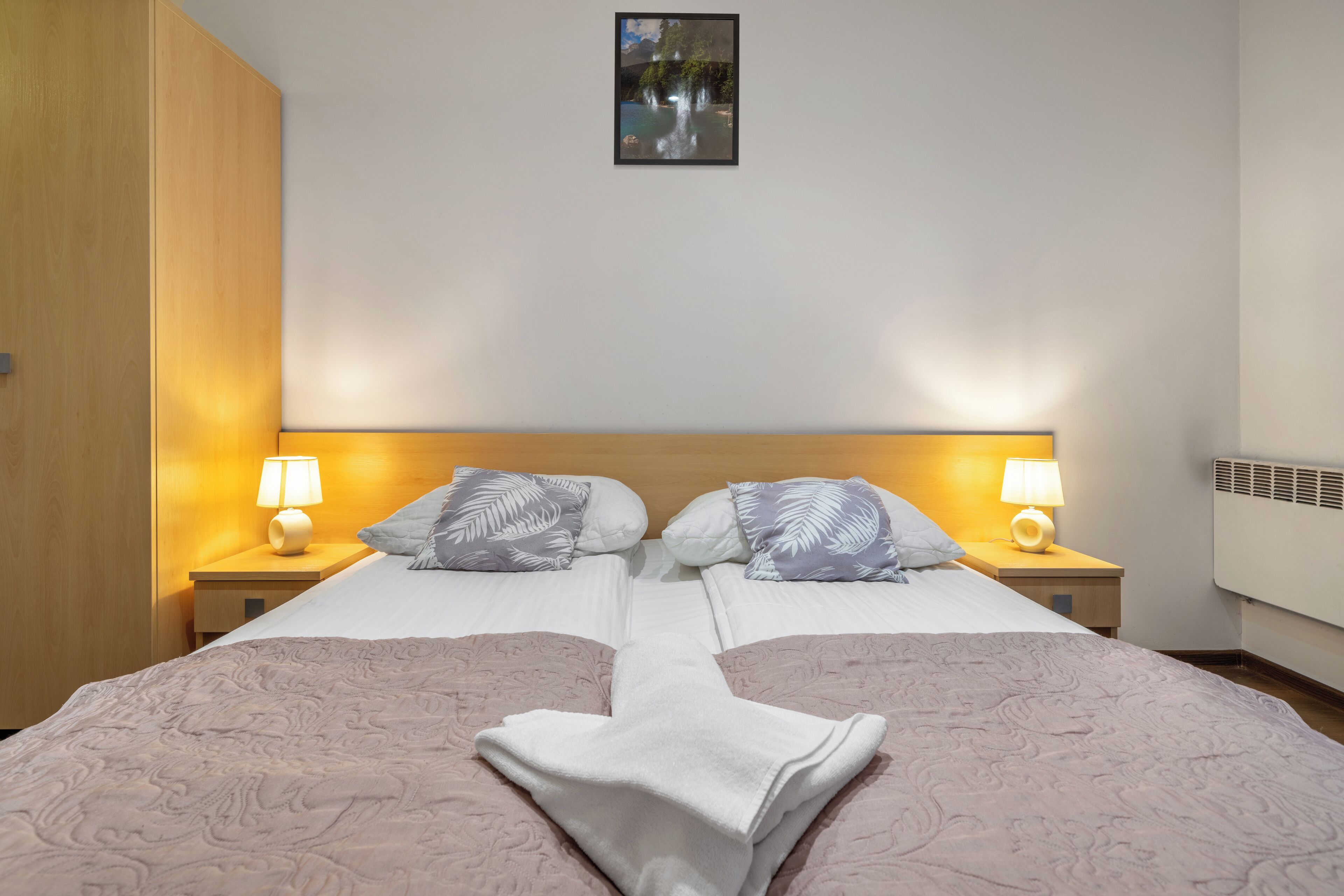 Una cama doble con una colcha estampada, dos mesitas de noche con lámparas, un cuadro enmarcado en la pared y un armario de madera.