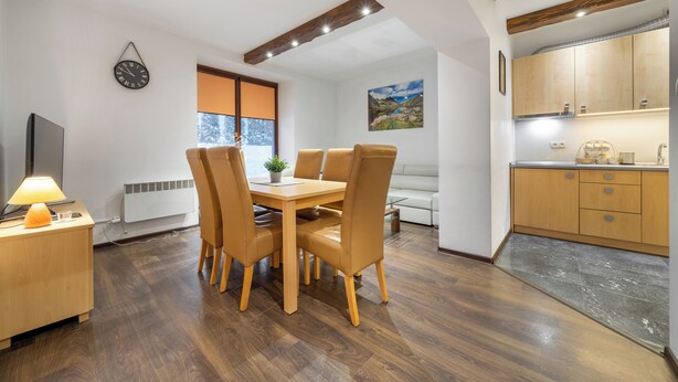 Una cocina moderna con armarios de madera, una zona de comedor con mesa y sillas, y un reloj fijado a la pared.