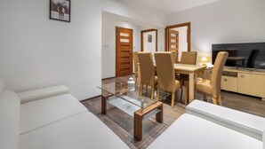Un comedor moderno con una mesa de vidrio, sillas de madera y un televisor al fondo.