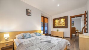 Un dormitorio con una cama grande, una mesita de noche con una lámpara, un aparador de madera y un espejo.
