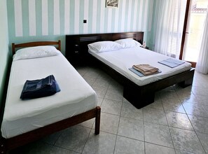 Una habitación con dos camas, cabecero de madera, suelo de baldosas y una ventana con cortinas.