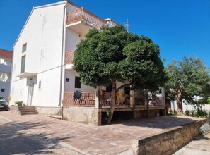 Un bâtiment à deux étages doté d’un balcon, avec un arbre devant et une zone pavée.