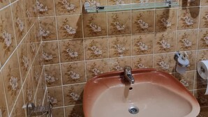 A bathroom with a beige sink, a faucet, a toilet paper holder, and a shower caddy on a tiled wall with a floral pattern. - Apartments Željka - Studio Apartment with Terrace (Orebic)