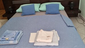 A neatly made bed with a blue bedspread, two pillows, and a stack of folded towels. - Apartments Željka - Studio Apartment with Terrace (Orebic)