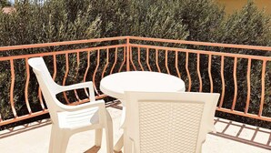 Un balcon avec une table ronde blanche et deux chaises blanches, entouré d’une rambarde en métal.