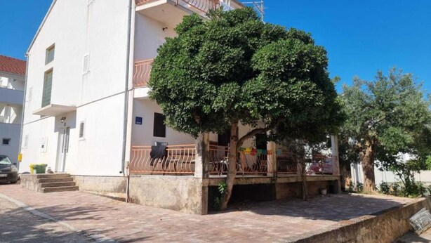 Un bâtiment à deux étages doté d’un balcon, avec un arbre devant et une zone pavée.
