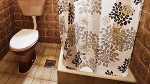 Une salle de bain avec des toilettes, un rideau de douche à motifs floraux et des murs carrelés.
