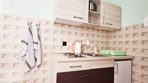 Une cuisine de taille réduite, équipée d’un évier, d’une cuisinière, d’un réfrigérateur et d’un placard au-dessus du plan de travail.