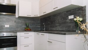 A modern kitchen with white cabinetry, a stainless steel oven, and a dark backsplash.