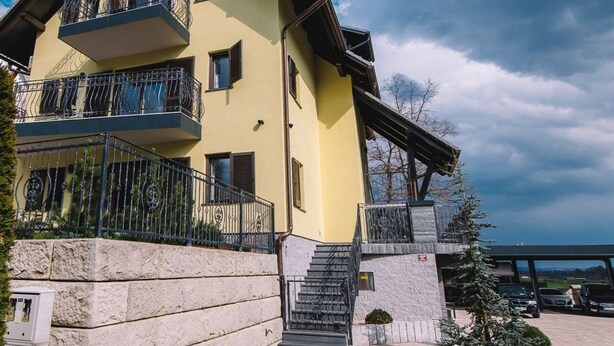 A multi-story yellow building with balconies, a stone base, and a staircase leading to the entrance.