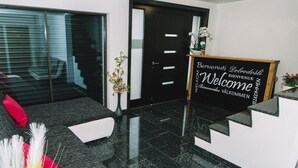 A modern reception area with a black reception desk, a welcome sign, and a sofa with decorative pillows. - Bled Prestigious and Stylish Apartments - Standard One Bedroom Apartment with Balcony (Bled)