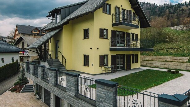 A multi-story yellow building with a balcony, a stone facade, and a paved driveway. - Bled Prestigious and Stylish Apartments - Standard One Bedroom Apartment with Balcony (Bled)