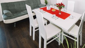 Un coin repas avec une table blanche, un set de table rouge, des chaises blanches et un canapé gris.