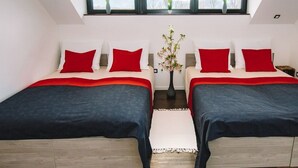 Une chambre avec deux lits, chacun agrémenté de draps rouges et bleus, un tapis blanc et un vase de fleurs posé sur une table de chevet.