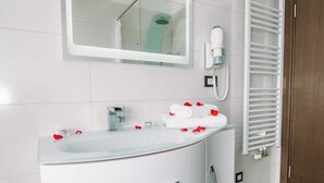 Une salle de bain moderne avec un lavabo en verre, une douchette à main, un porte-serviettes avec des serviettes et un sèche-serviettes blanc.