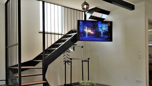 A modern interior with a curved staircase, a mounted TV, and a minimalist decor including a plant and candle.