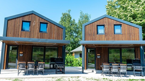 Two modern wooden houses with large windows and outdoor seating areas.