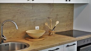 A kitchen with a stainless steel sink, wooden countertop, white cabinets, and a built-in oven.