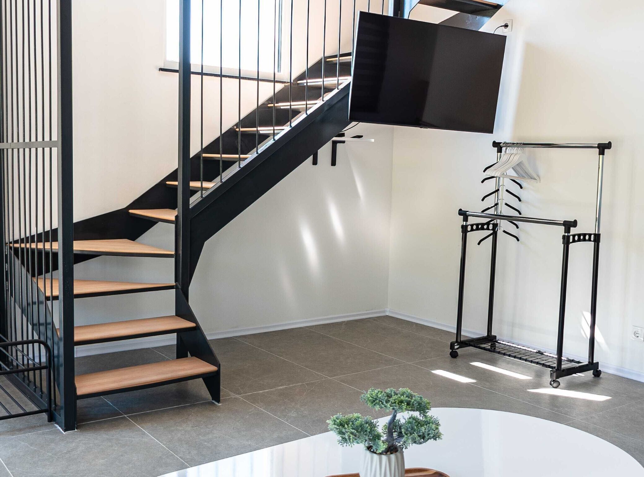 Un intérieur moderne avec un escalier en colimaçon noir, un téléviseur fixé au mur et une petite plante en pot posée sur une table blanche.