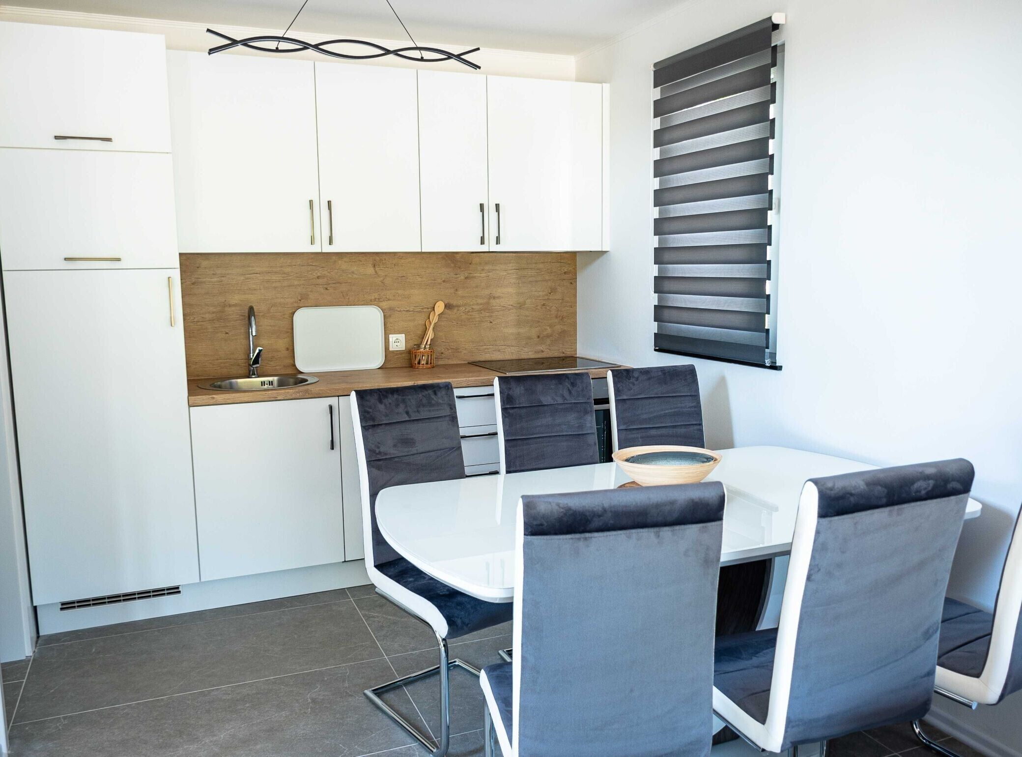 Une cuisine moderne avec des meubles blancs, un plan de travail en bois et un coin repas comprenant une table blanche et des chaises à revêtement gris.