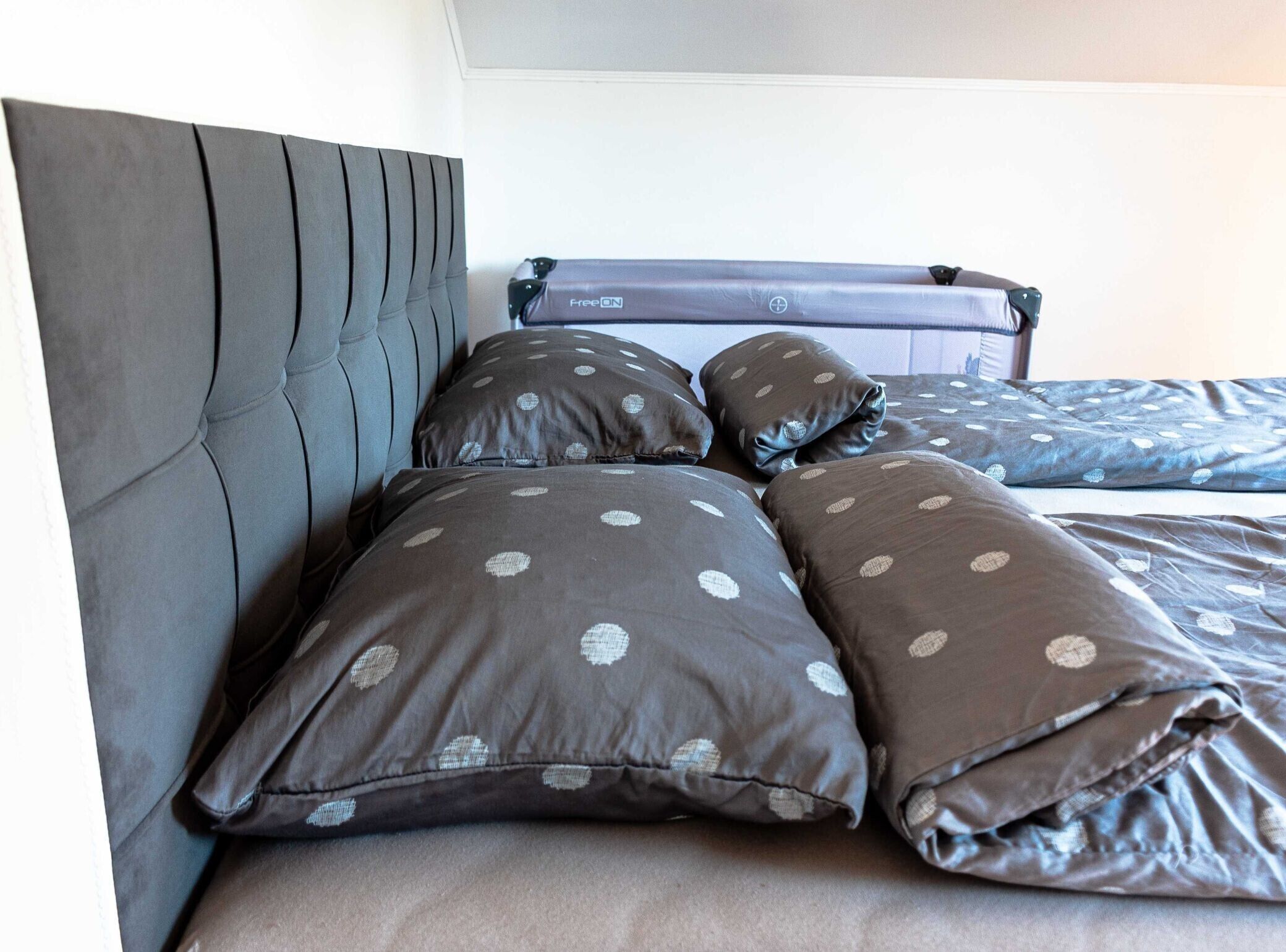 A bed with a headboard, multiple pillows with a polka dot pattern, and a blue blanket.