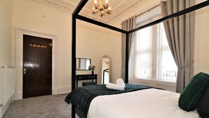 A four-poster bed with a dark frame, a white comforter, and a green throw blanket. There is a dark wooden door with a mirror above it, and a window with curtains on the right. - Private 10 Bedrooms Detached Villa in Glasgow | Pool Table | Garden | Piano (Glasgow)