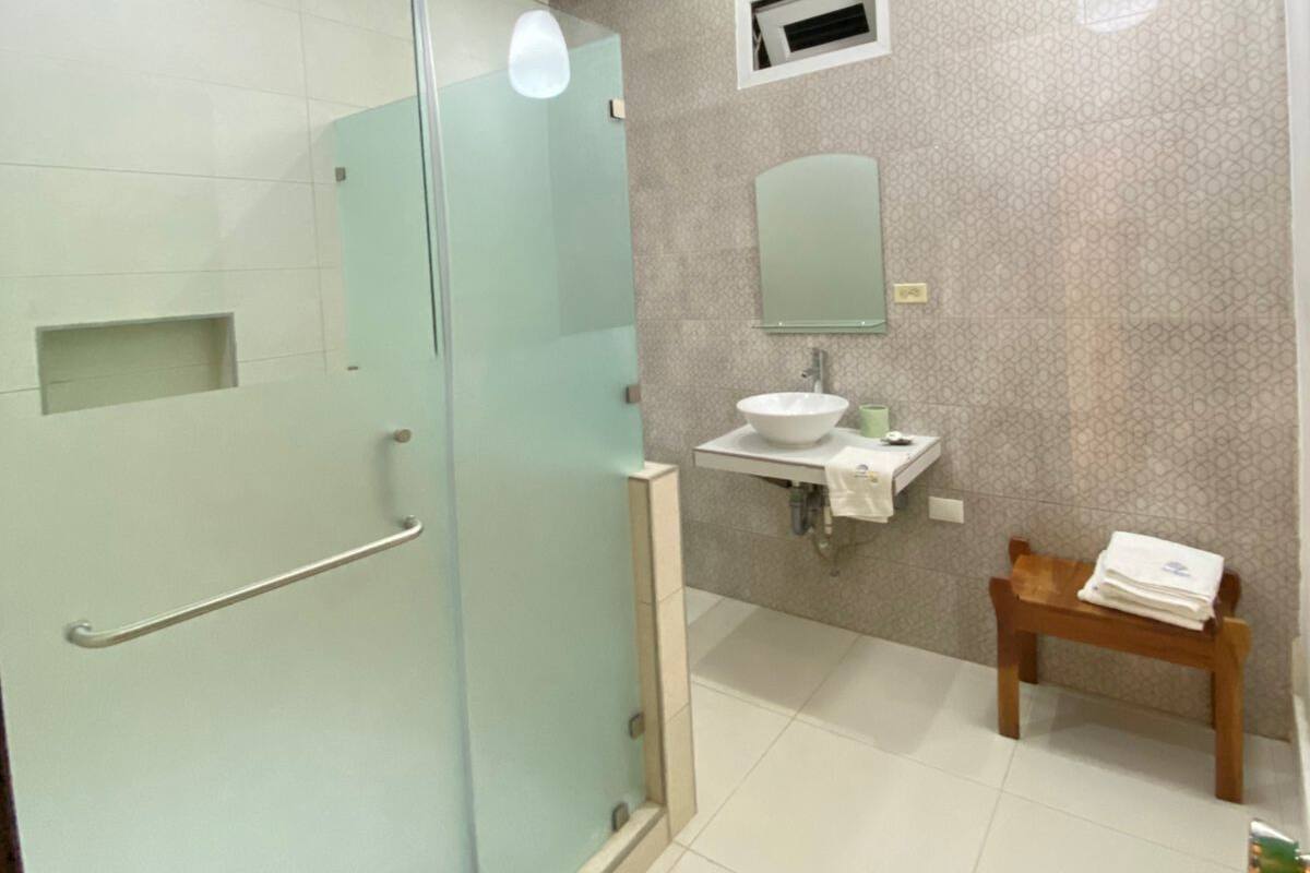A modern bathroom with a glass shower enclosure, a sink with a mirror, and a wooden chair.