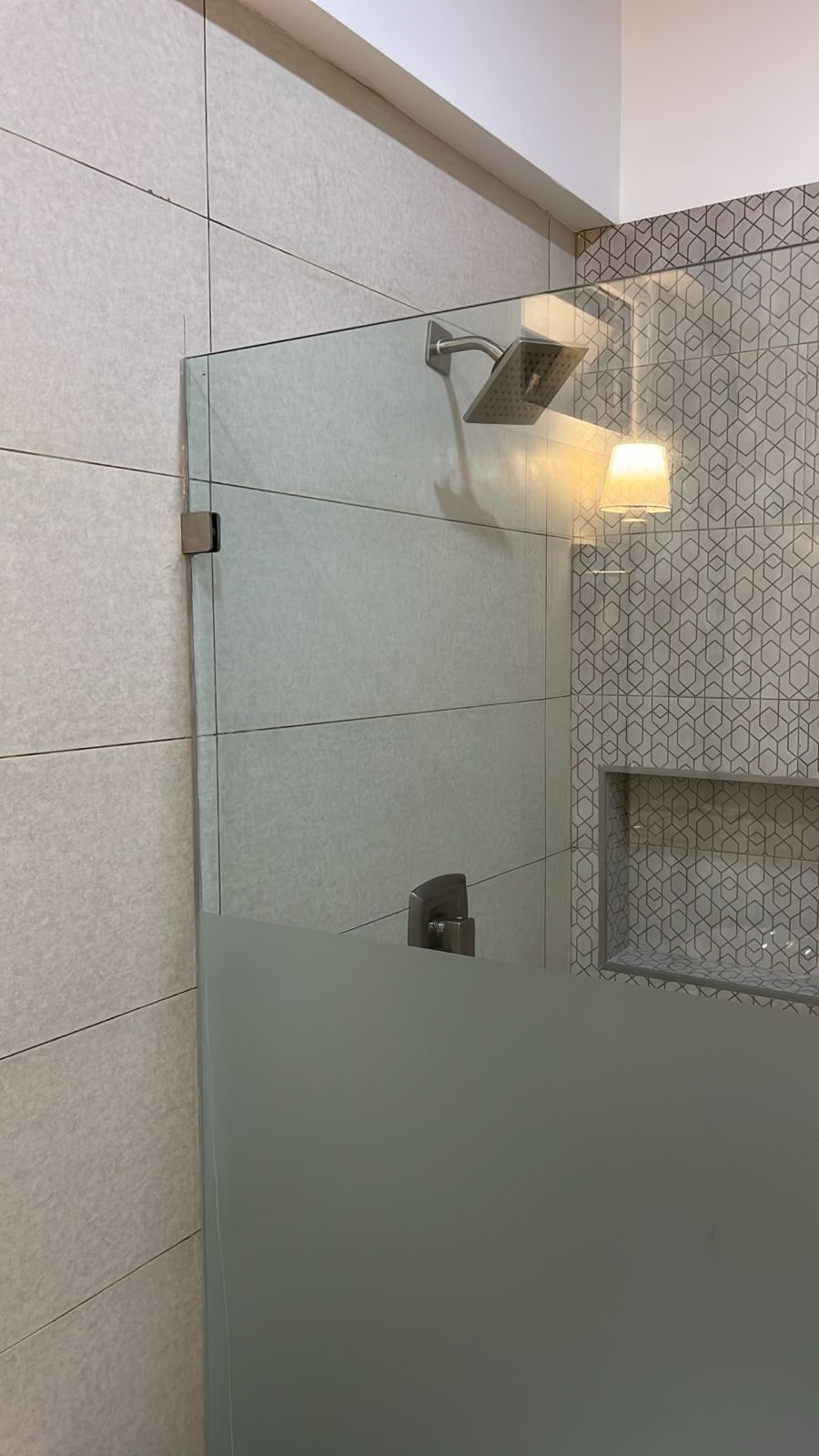 Un baño con cabina de ducha de vidrio, toallero de pared y salpicadero de azulejos con diseño geométrico.