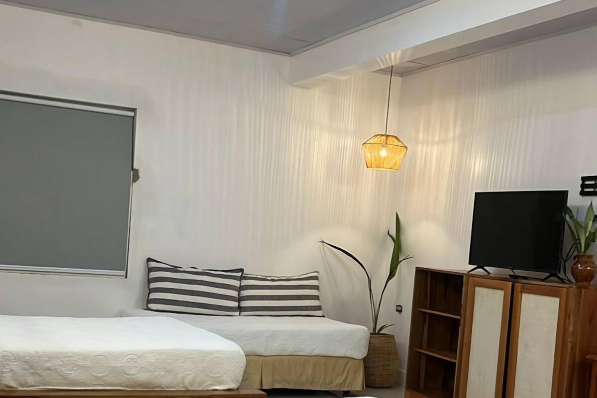A modern bedroom with two beds, a television, and a decorative hanging light fixture.