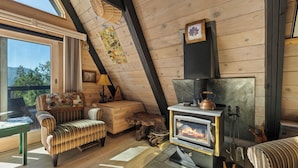 Interior acogedor de una cabaña con techo de madera, chimenea, mobiliario a rayas y vistas amplias a través de grandes ventanales.