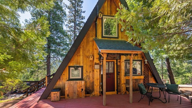 Una cabaña de madera con terraza roja, una puerta principal y un pequeño porche con mesa y sillas.