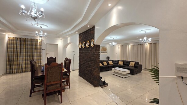 A modern living room with a dining area, featuring a stone fireplace, a sectional sofa, and elegant chandeliers.
