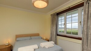 Une chambre à coucher avec un lit, deux tables de chevet, une fenêtre avec des rideaux et une vue sur l’extérieur.