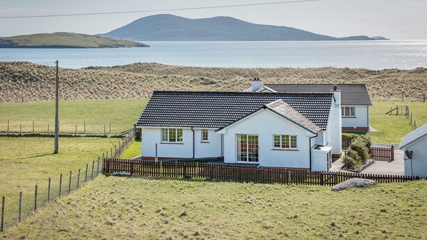 Une maison située sur la côte, dotée d’une cour clôturée et offrant une vue sur la mer et les collines.