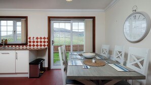 Une cuisine avec un coin repas, une grande horloge au mur et une vue sur l’extérieur.