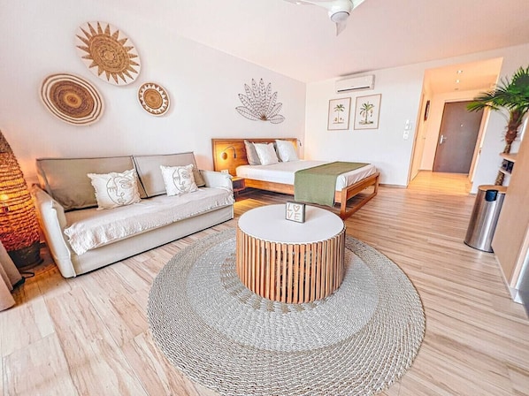 A modern living room with a round wooden coffee table, a sofa, a bed, and a small round table with a 'LOVE' sign. - Alamanda 7 - accès direct plage Orient Bay (Orient Bay)