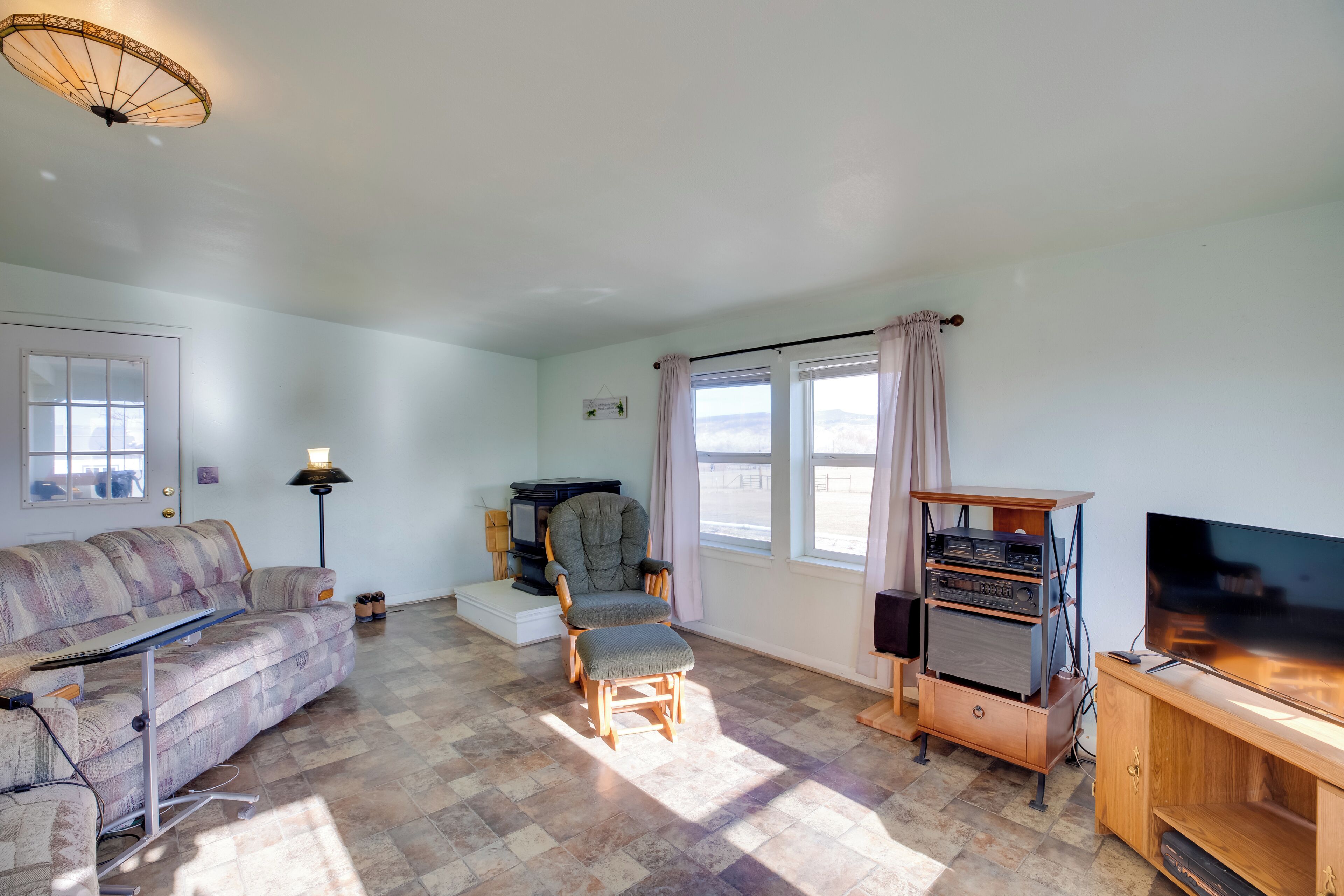 Un salon comprenant un canapé, un fauteuil, un pouf, un meuble pour la télévision et un ventilateur de plafond.