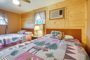 A cozy cabin-style room with two beds, a nightstand with a lamp, and a window with curtains.
