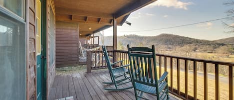 Una terraza de madera con mecedoras y vistas a un paisaje montañoso.