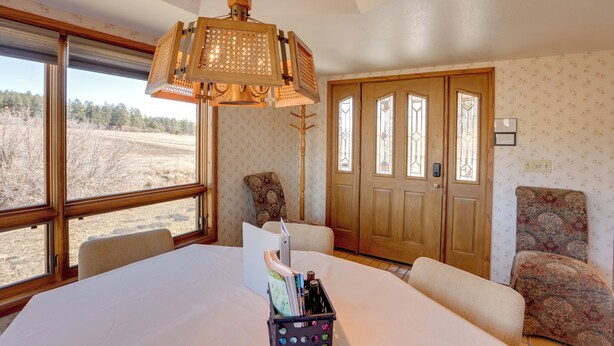 A room with a large bed, a wooden door, a chair, and a view of a field through large windows. - Mtn-View Retreat Near Hiking in Bayfield! (Bayfield)