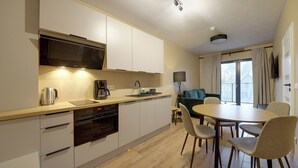 A modern kitchen with a built-in oven, microwave, and coffee maker. There is a dining area with a round table and chairs. - RentPlanet - Apartament Belle View (Szklarska Poreba)